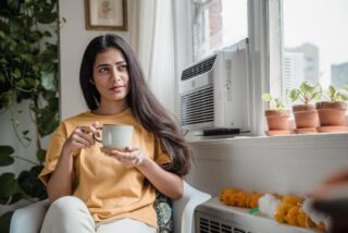 Vrouw die voor airco en verwarming koffie aan het drinken is